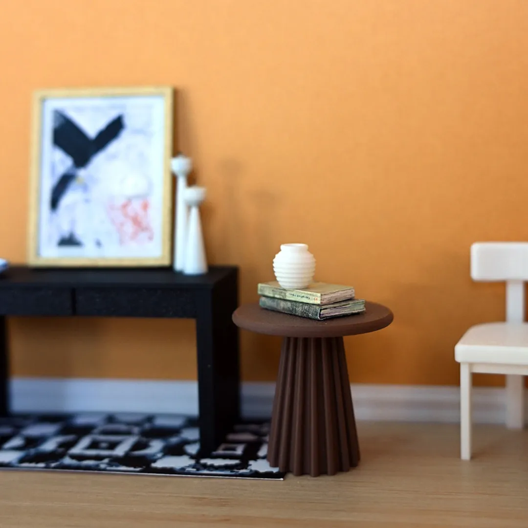 A scene of mini furniture, including a brown side table, black console table with a painting and tall white candles, and a white chair, against an orange wall