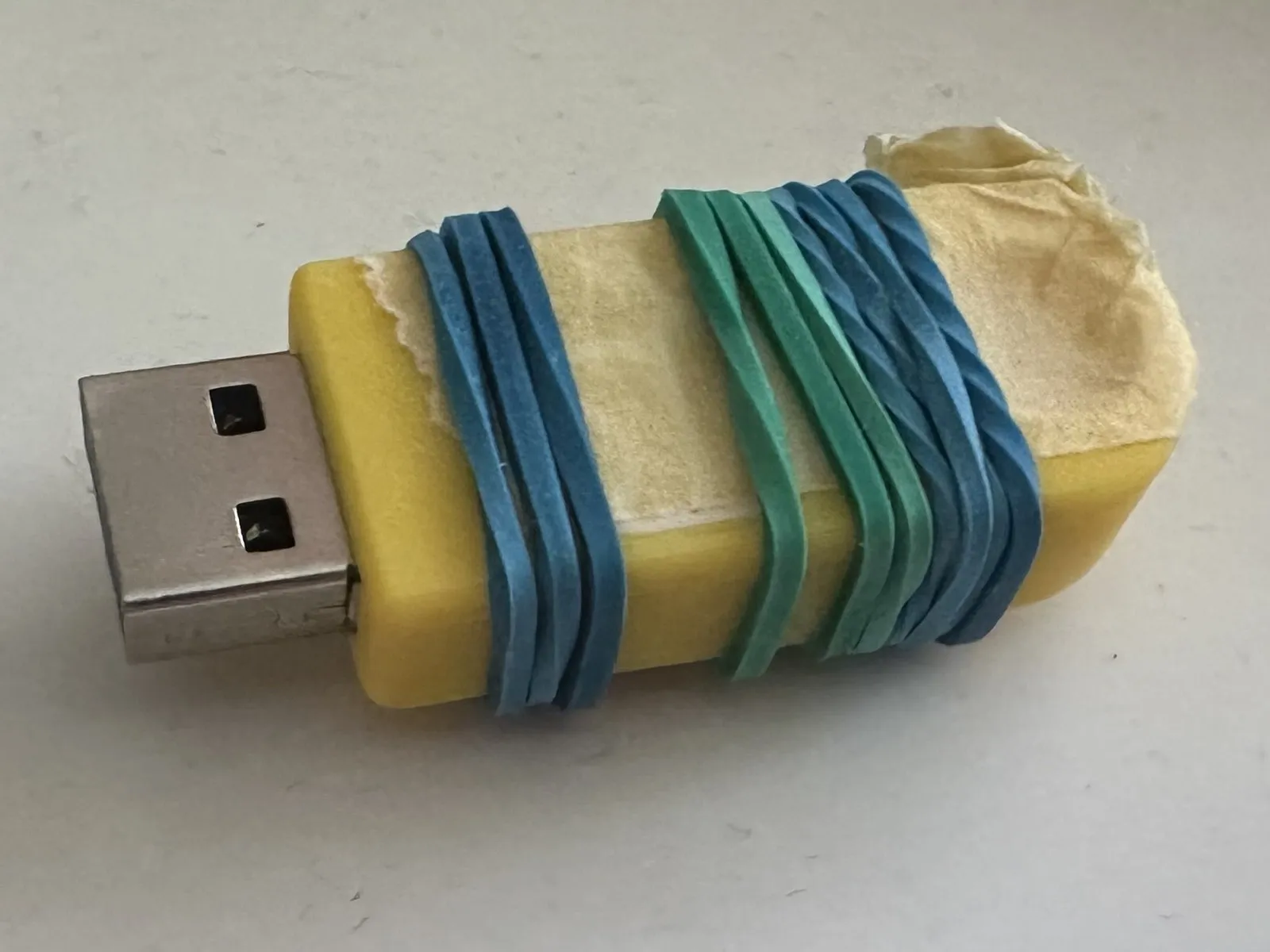 Thumb drive cover being held in place with painters tape and rubber bands while superglue is hardening