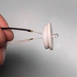 A hand holding a small white light bulb

Description automatically generated