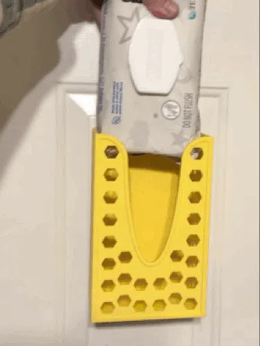 An action shot of a pack of wipes being dropped into the top of the mounted dispenser. The image highlights the structural rigidity of the frame and the secure grip of the magnetic base during loading.