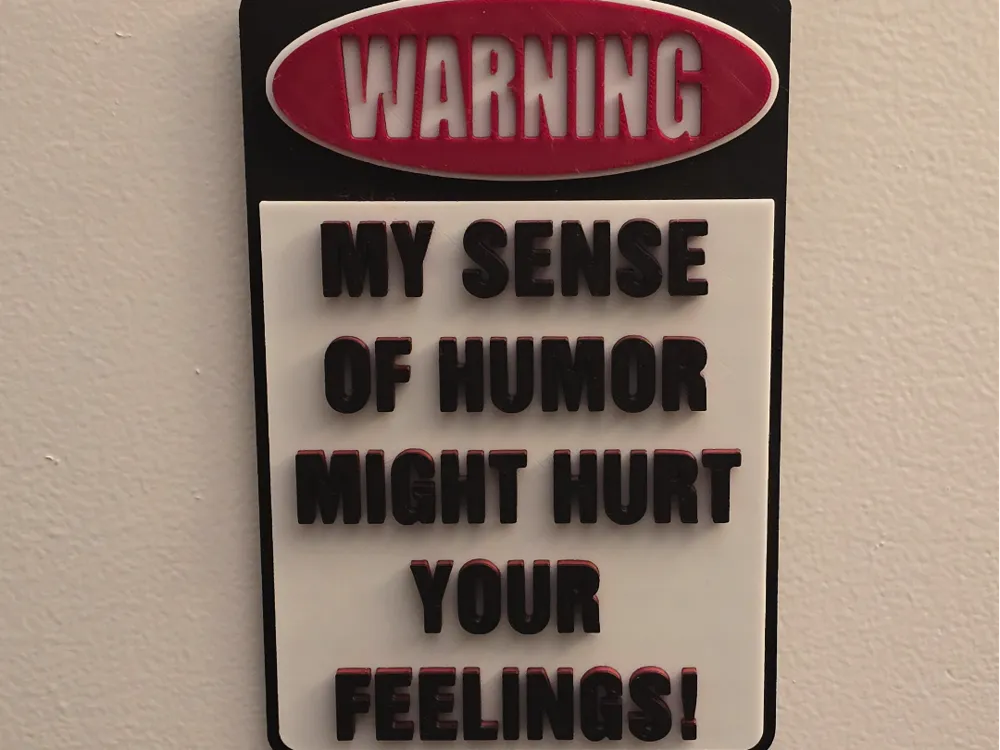 Letrero o emblema decorativo: Warning - Sense of Humor Version. Referencia del modelo original.