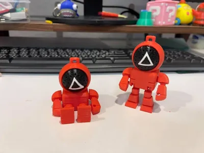 Squid Game figures with movable limbs and rotatable masks, requiring color separation printing and assembly